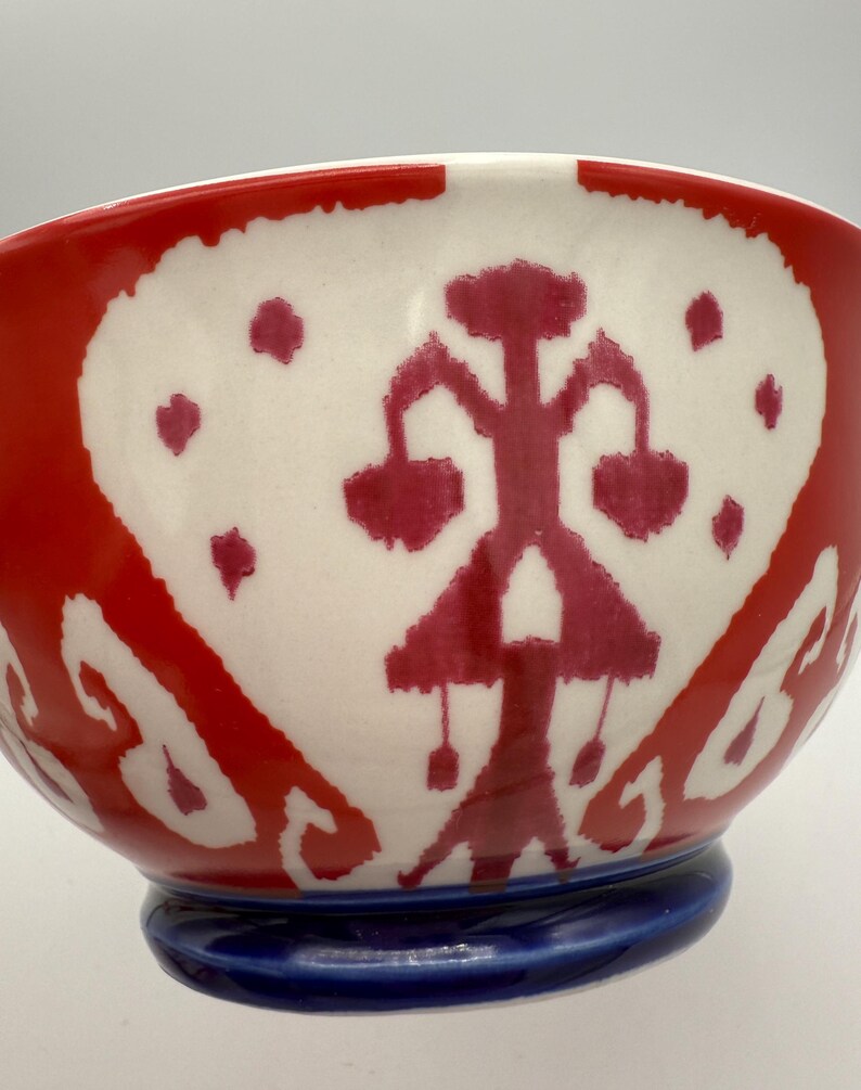 May include: A ceramic bowl with a red and white design. The bowl features a red exterior with a white interior, adorned with a red abstract pattern. The base is a solid blue color. The bowl is a decorative piece.