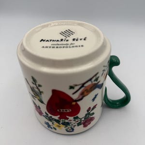 May include: White ceramic mug with a green handle, featuring a red heart with the word "LOVE" and floral and bird illustrations. The bottom of the mug has the text "Nathalie Lete" and "exclusively for Anthropologie".