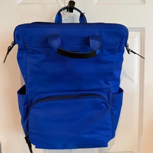 May include: A vibrant blue backpack with multiple compartments and a top handle. The backpack features a front zippered pocket, side pockets, and adjustable straps. The bag is made of a durable, water-resistant material.