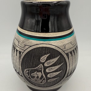 May include: A black and silver ceramic vase with a bear paw design. The vase has a black top, a turquoise stripe, and a detailed bear paw and tribal pattern. The vase is approximately 6 inches tall.