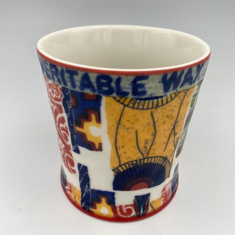 K&ouml;nnte beinhalten: Eine wei&szlig;e Keramiktasse mit einem geometrischen Muster in Rot, Blau und Gelb. Die Tasse tr&auml;gt den Schriftzug "VERITABLE WAX" auf der Seite.