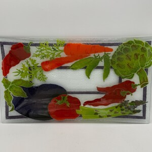 May include: Rectangular glass serving dish with a decorative vegetable design. The design includes a red chili pepper, carrots, green peas, an artichoke, a tomato, an eggplant, and asparagus. The dish has a black and white border.