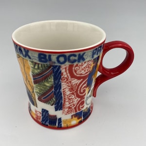 K&ouml;nnte beinhalten: Eine rote und wei&szlig;e Keramiktasse mit einem bunten Muster. Die Tasse hat einen roten Griff und der Text "Max Block Print" ist an der Seite sichtbar.
