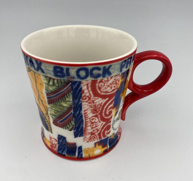 K&ouml;nnte beinhalten: Eine rote und wei&szlig;e Keramiktasse mit einem bunten Muster. Die Tasse hat einen roten Griff und der Text "Max Block Print" ist an der Seite sichtbar.