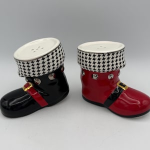 May include: A pair of ceramic salt and pepper shakers shaped like boots. One is black with a red strap and gold buckle, the other is red with a black strap and gold buckle. Both have a white and black houndstooth pattern at the top.