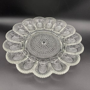 May include: A clear glass egg plate with a textured surface and 12 individual compartments for serving eggs.