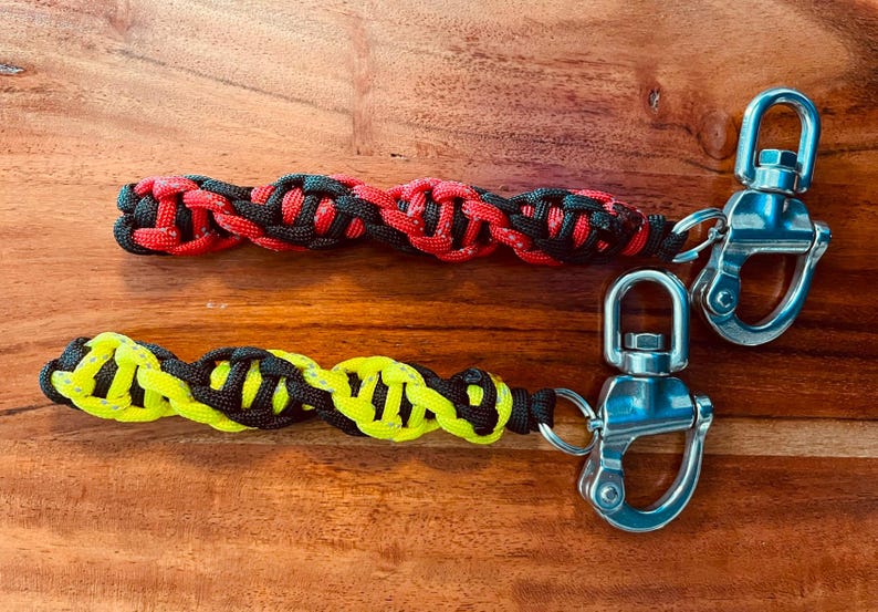 May include: Two paracord keychains. One is red and black, the other is yellow and black. Each keychain features a braided design and a silver swivel clasp for easy attachment to keys or bags.