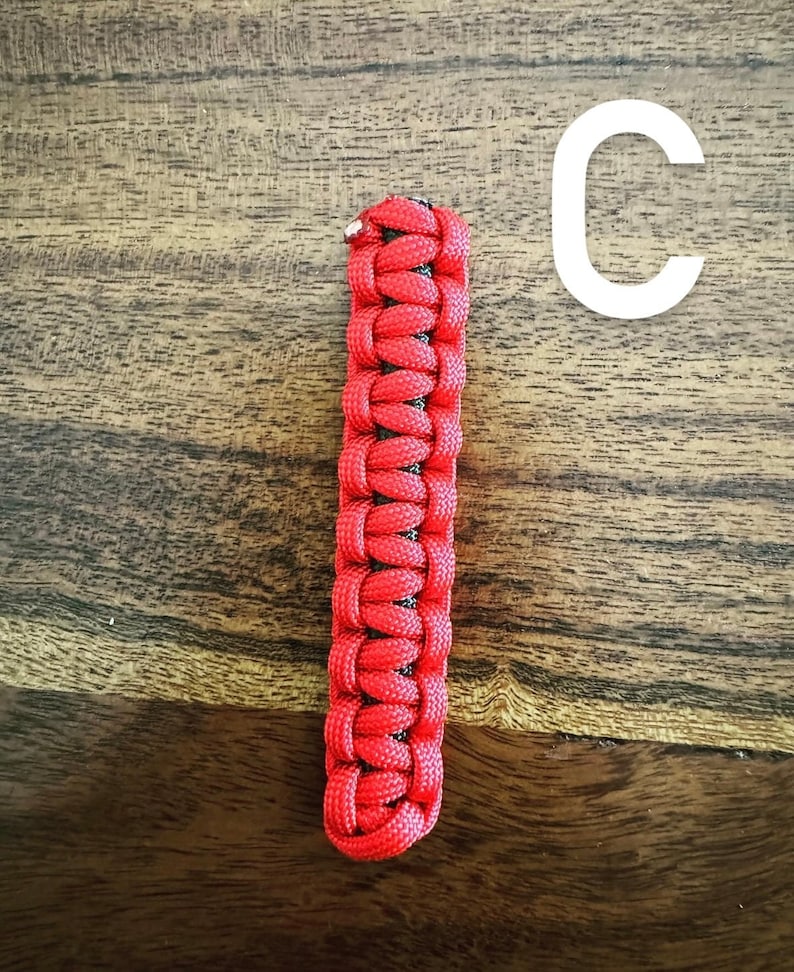 May include: A red and black woven paracord keychain fob. The fob is rectangular and features a tight weave pattern. The letter "C" is in white in the background.
