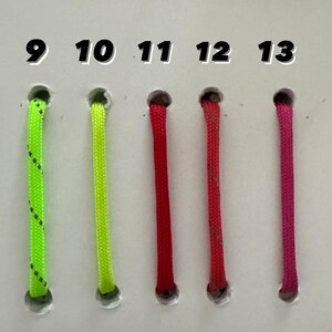 May include: A selection of colorful cords, each emerging from a hole and labeled with a number from 8 to 14. The cords are green, neon green, red, and pink, with a black and white pattern on one. The cords are likely for crafting or jewelry making.