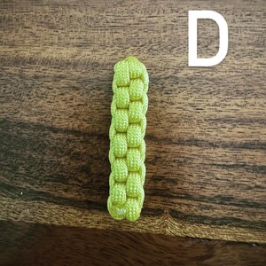 May include: A lime green, woven paracord keychain fob. The fob is rectangular and features a tight, basket-weave pattern. The background is a dark, wooden surface with visible grain.