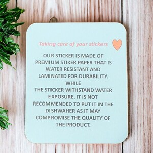 Op de afbeelding: Een lichtblauwe vierkante sticker met een roze hart in de rechterbovenhoek. De sticker heeft tekst die luidt: "Zorg voor je stickers. Onze sticker is gemaakt van premium stickerpapier dat waterbestendig is en gelamineerd voor duurzaamheid. Hoewel de sticker waterbestendig is, wordt het niet aanbevolen om hem in de vaatwasser te doen, omdat dit de kwaliteit van het product kan aantasten."