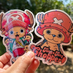 May include: Two holographic stickers featuring Tony Tony Chopper from the anime One Piece. The stickers are red and white with a cartoon image of Chopper in his reindeer form. The text "Tony Tony Chopper" is written in a red and white font on the sticker.