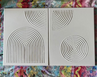 May include: Two-panel white canvas art with textured, raised designs. One panel features a half-circle and a full arch, while the other has a half-circle and a spiral. The artwork is a modern, minimalist design.