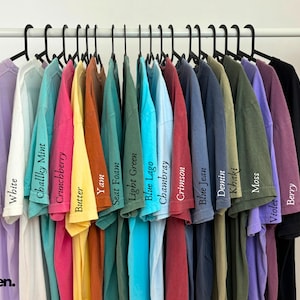 May include: A rack of 18 t-shirts in various colors, including orchid, white, chalky mint, crunchberry, butter, yam, seat foam, light green, blue lago, chambray, crimson, blue jean, denim, khaki, moss, violet, berry, and black.