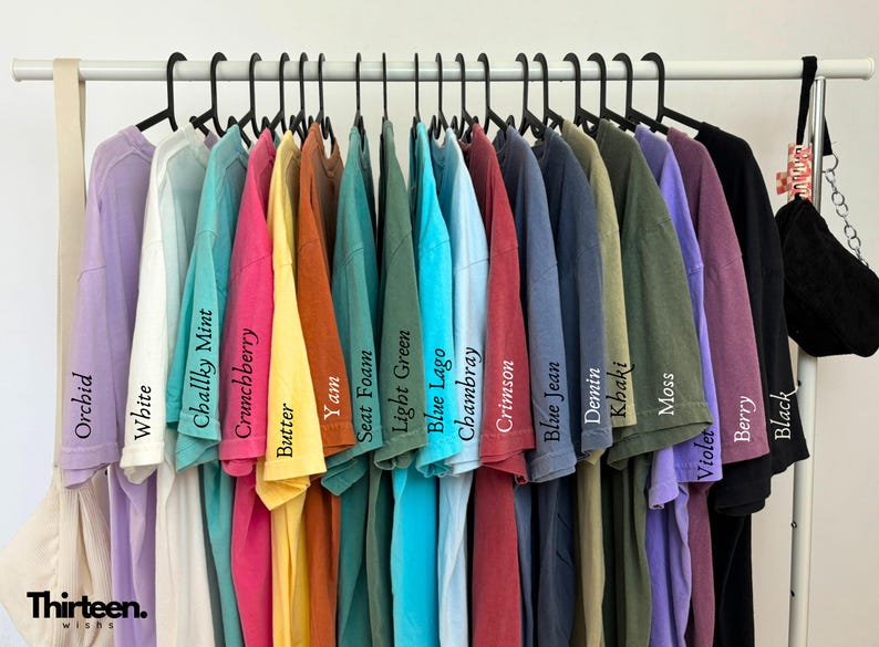 May include: A rack of 18 t-shirts in various colors, including orchid, white, chalky mint, crunchberry, butter, yam, seat foam, light green, blue lago, chambray, crimson, blue jean, denim, khaki, moss, violet, berry, and black.