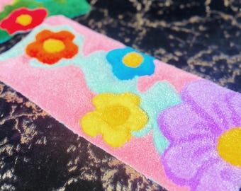 May include: A pink rug with a colorful flower design. The rug features yellow, blue, orange, and purple flowers.