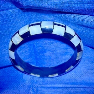 May include: A black and white checkered bangle bracelet made of polished bone or shell.