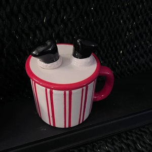 May include: A red and white striped ceramic mug with a black and white Santa boot lid. The mug has a red handle.