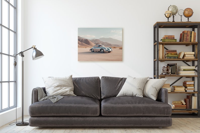 An original color car poster featuring the iconic Porsche 356 in silver in a desert. Available in  multiple sizes with free shipping. Pictured in a frame above a sofa. (frame not included)
