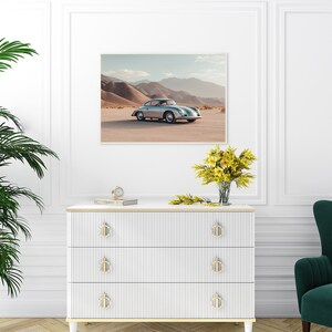 An original color car poster featuring the iconic Porsche 356 in silver in a desert. Available in  multiple sizes with free shipping. Pictured in a frame above a set of drawers. (frame not included)