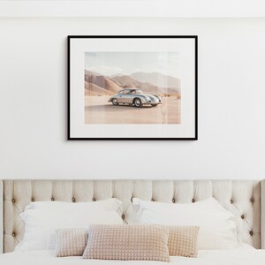 An original color car poster featuring the iconic Porsche 356 in silver in a desert. Available in  multiple sizes with free shipping. Pictured in a frame above a bed. (frame not included)