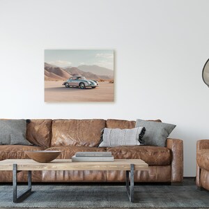 An original color car poster featuring the iconic Porsche 356 in silver in a desert. Available in  multiple sizes with free shipping. Pictured in a frame above a sofa. (frame not included)