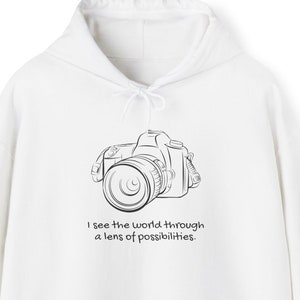 May include: White hoodie with a black outline of a camera and the text "I see the world through a lens of possibilities."