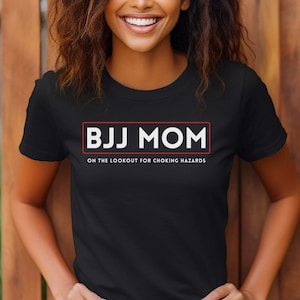 May include: Black t-shirt with white text that reads "BJJ MOM ON THE LOOKOUT FOR CHOKING HAZARDS" in a red rectangle.