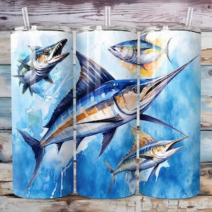 Pode incluir: Um conjunto de três copos de aço inoxidável com um design de aquarela de vários peixes, incluindo um marlin, um atum e uma barracuda. Os copos são azuis, amarelos e brancos.