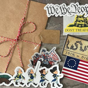 May include: A selection of stickers and a brown paper package tied with red and white twine. Stickers include the phrase "We the People", a coiled snake with "Don't Tread on Me", and a flag with 13 stars. Also, a sticker with the phrase "Join, or Die".