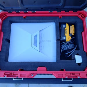 May include: A red, rectangular, hard-shell case with a black interior. Inside, there's a white electronic device, a yellow and black battery, and a black cord. The case is open, revealing the contents.