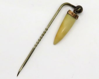 May include: A gold pin with a white tooth-shaped charm. The pin is twisted and has a small gold ball at the top.