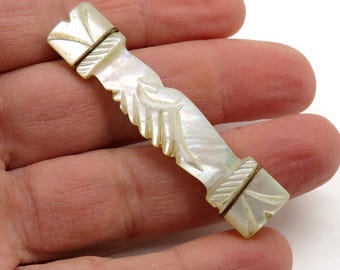 Puede incluir: Una barra tallada de nácar iridiscente con extremos geométricos y un diseño central estilizado. La barra se sostiene en una mano, mostrando sus intrincados detalles y brillo nacarado. La barra mide aproximadamente 7.6 cm de largo.