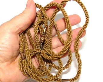 May include: A long, brown, braided cord necklace with copper accents. The cord is made of a soft, woven material and has a subtle sheen.