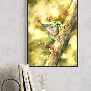 Puede incluir: Pintura a la acuarela de una vibrante rana arbórea verde con patas y ojos rojos, posada en una rama marrón. La obra de arte está enmarcada en un borde negro, sobre un fondo de acuarela amarillo y verde.