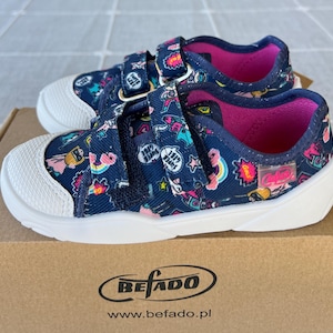 May include: A pair of blue and white sneakers with colorful patches and a pink lining. The sneakers have velcro straps and a white sole. The box has the text "Befado" and "www.befado.pl" printed on it.