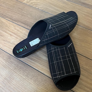 May include: A pair of black open-toe slide sandals featuring a white grid pattern on the upper strap. The footbed is black with a white label displaying the text BIO and a blue cross symbol. The brand name Adonex is printed on the side of the strap.
