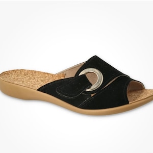 May include: Black slide sandal with a cork footbed and a tan sole. The sandal features a black strap with a silver-colored metal ring detail. The adjustable strap secures with a hook-and-loop closure.