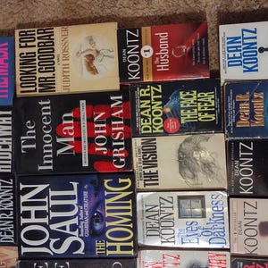 K&ouml;nnte beinhalten: Eine Sammlung von Taschenb&uuml;chern, die in einem Raster angeordnet sind, mit Titeln von Dean Koontz, John Grisham und John Saul. Sichtbare Titel sind unter anderem The Mask, Looking for Mr. Goodbar, The Husband, The Key to Midnight, Hideaway und The Homing.