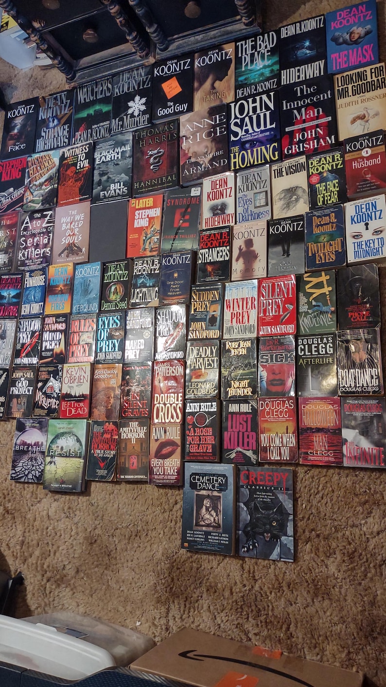 K&ouml;nnte beinhalten: Eine gro&szlig;e Sammlung von Taschenb&uuml;chern aus den Bereichen Thriller und Horror, die in einem Raster an einer Wand angeordnet sind. Die B&uuml;cher zeigen verschiedene Titel und Autoren wie Dean Koontz, John Sandford und Douglas Clegg mit bunten Covern.