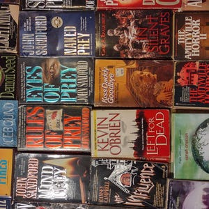 K&ouml;nnte beinhalten: Eine Sammlung verschiedener Taschenb&uuml;cher aus den Bereichen Thriller und Horror, die in einem Raster angeordnet sind. Sichtbare Titel sind unter anderem Lightning, Naked Prey, In Silent Graves, The Amityville Horror II, Demon Seed, Eyes of Prey und Icebound.