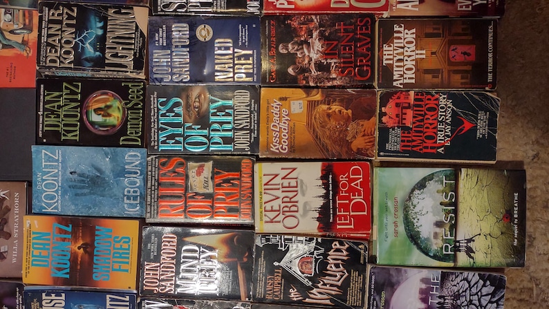 K&ouml;nnte beinhalten: Eine Sammlung verschiedener Taschenb&uuml;cher aus den Bereichen Thriller und Horror, die in einem Raster angeordnet sind. Sichtbare Titel sind unter anderem Lightning, Naked Prey, In Silent Graves, The Amityville Horror II, Demon Seed, Eyes of Prey und Icebound.