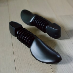 May include: Two black shoe trees with a ribbed design. The shoe trees are made of plastic and have a rounded shape.