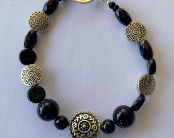 Puede incluir: Pulsera negra y plateada con cierre de palanca. La pulsera presenta cuentas negras y dijes plateados con un diseño de estrella.