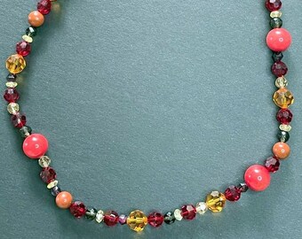 Puede incluir: Un collar hecho de cuentas rojas, naranjas y marrones. El collar tiene un cierre plateado.