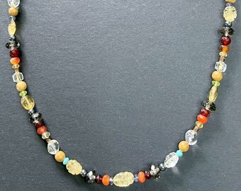 Puede incluir: Un collar de cuentas multicolores con cierre magnético. El collar presenta cuentas en tonos de marrón, naranja, amarillo, verde, azul y gris.