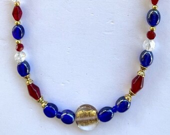 Puede incluir: Un collar de cuentas rojas, blancas y azules con un colgante de vidrio con hoja de oro.