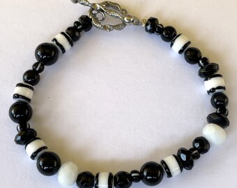 Puede incluir: Pulsera de cuentas negras y blancas con cierre de palanca plateado. La pulsera presenta cuentas redondas negras y blancas, cuentas facetadas negras y cuentas blancas con rayas negras.