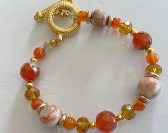 Puede incluir: Un brazalete de tono dorado con cuentas de cornalina, cuentas marmoleadas blancas y marrones y cuentas de vidrio transparentes y ámbar.