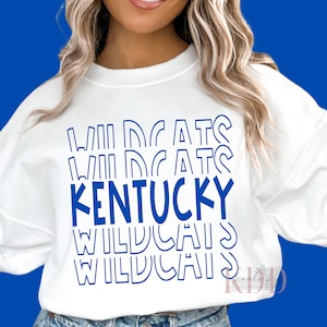 Pode incluir: Camisola branca com um design gráfico azul que diz "Wildcats Kentucky Wildcats Wildcats" em uma fonte retro empilhada.